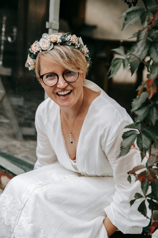Lachende Braut mit Blumenkranz und Brille
